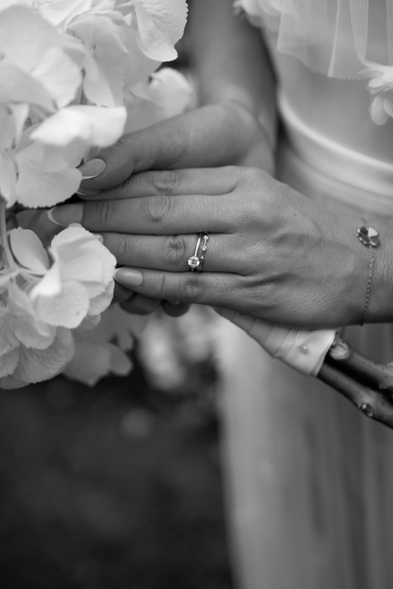 Brudens hand med ring mot en vit blomsterbukett — svartvitt
